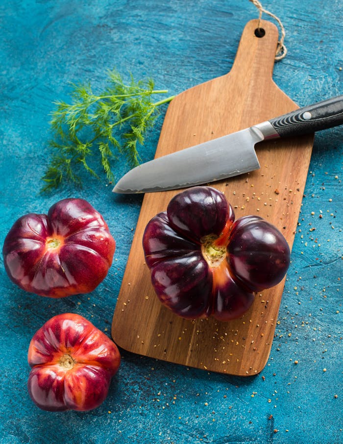 pexels-photo-2110485 Vibrant heirloom tomatoes with herbs and knife on a wooden board, perfect for food preparation visuals.