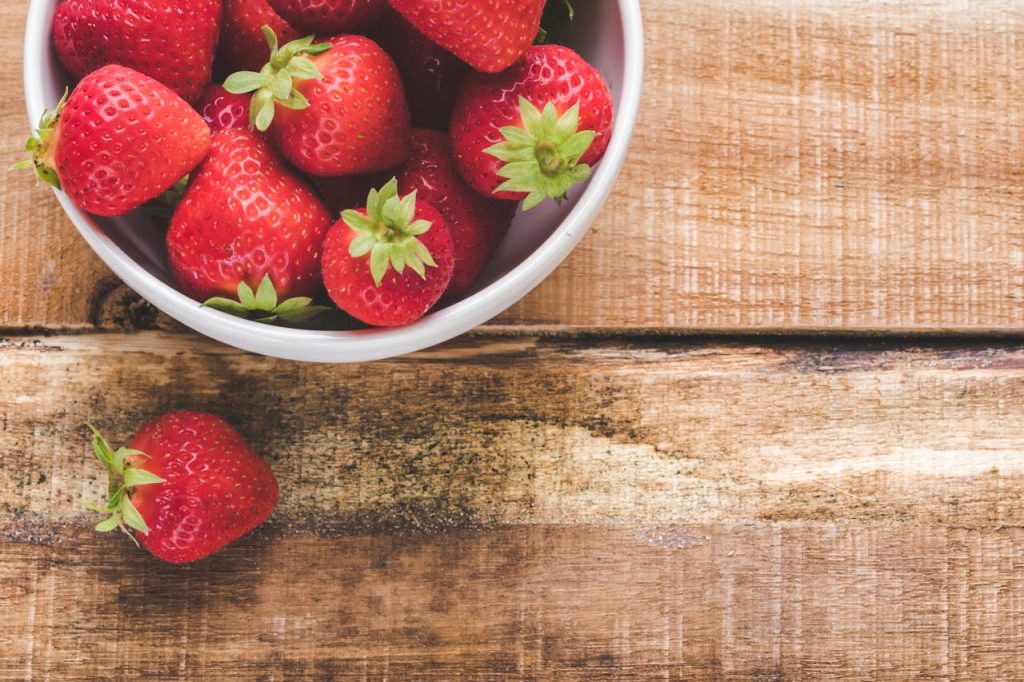 pexels-photo-2820142 Juicy red strawberries in a white bowl on a wooden table, showcasing freshness.