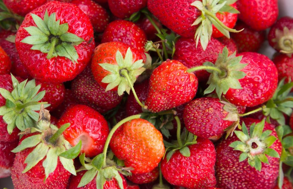 pexels-photo-35072889 Close-up view of vibrant fresh red strawberries with green leaves, highlighting juicy textures.